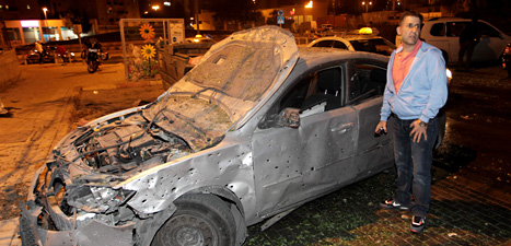 En israelisk man bredvid en bil som skadats av raketer. Foto:Ilan Assayag/Scanpix.