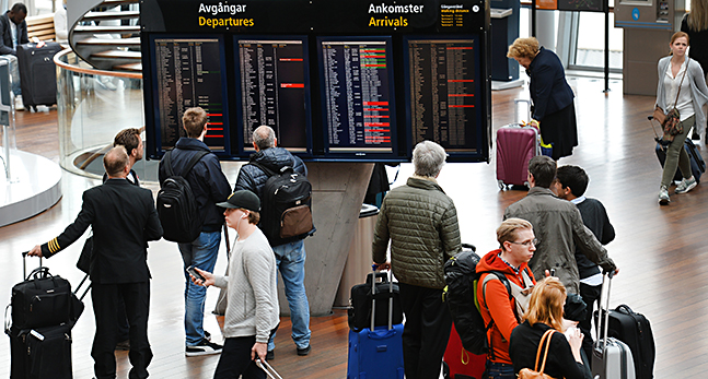Flera personer med resväskor står framför avgångs och ankomsttavlorna.