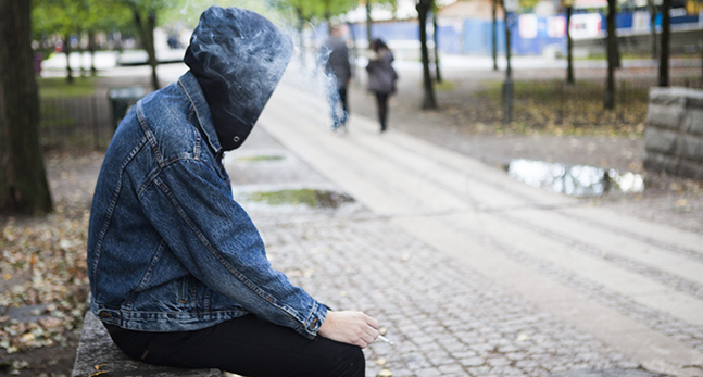 En ung person sitter på en bänk och röker.
