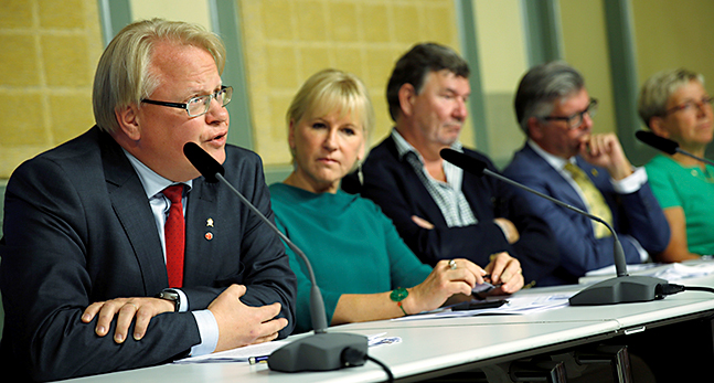 Peter Hultqvist sitter tillsammans med andra politiker vid ett långt bord.