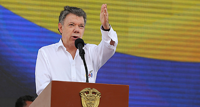 President Juan Manuel Santos står på ett podium och talar. Han har vit skjorta och sträcker ut en arm i luften.