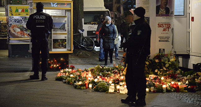 Poliser vaktar och bredvid finns många ljus och blommor.