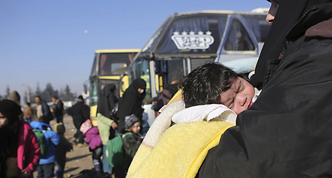 En kvinna bär ett barn vid bussarna som kört folk från Aleppo