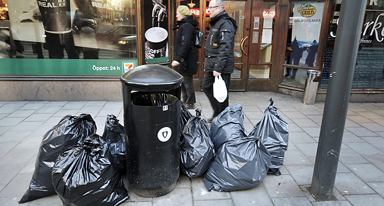Sopor på en gata i Stockholm. Stora svarta sopsäckar ligger slängda bredvid en papperskorg.