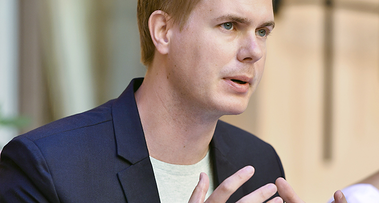 En bild på Gustaf Fridolin i vit t-shirt under en blå kavaj.