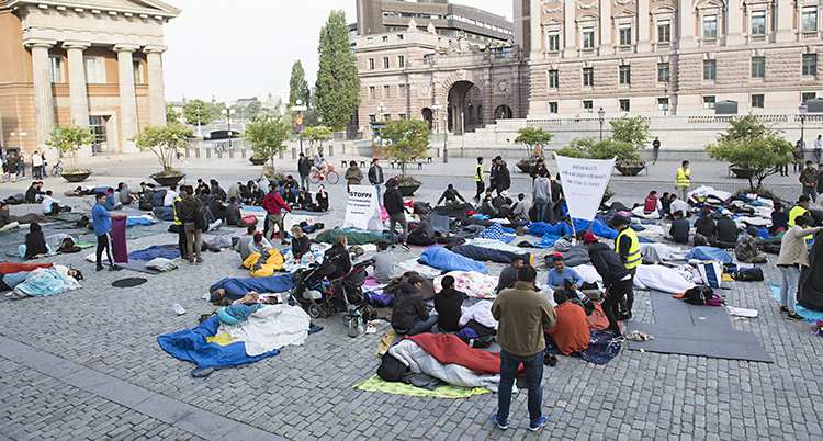 människor i sovsäckar sitter på marken på Mynttorget nära riksdagen i Stockholm.