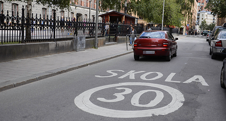 En bil kör förbi en skola. På gatan är markerat att det är 30 km i timmen som gäller som hastighet.