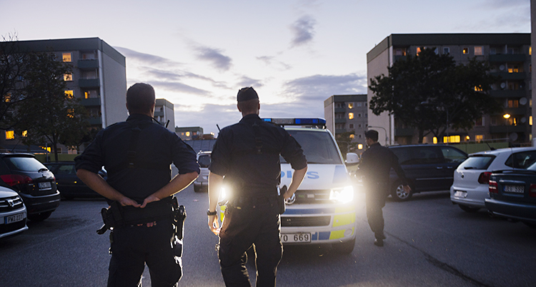 Två poliser står och tittar mot en gata.