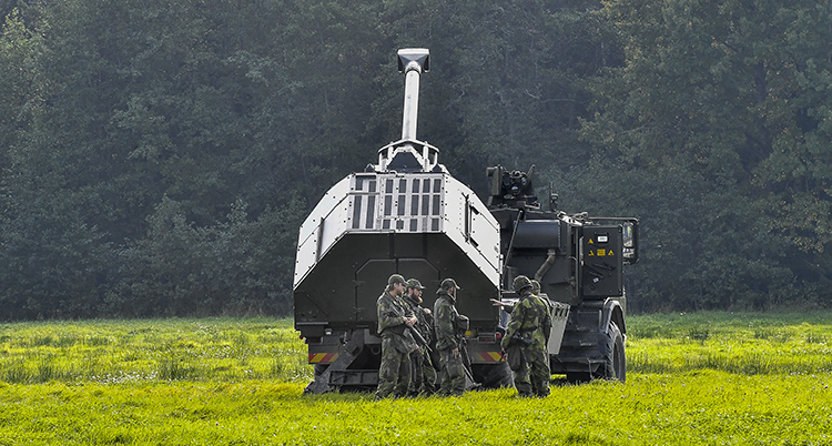 En svensk pansarvagn med soldater bredvid.