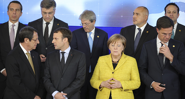 Flera länders ledare poserar för en bild. Alla tittar åt olika håll. Några pratar med varandra. Merkel tittar ner och ser besvärad ut. Bilden är troligen tagen medan politikerna fortfarande håller på att göra sig klara för att bli fotograferade.