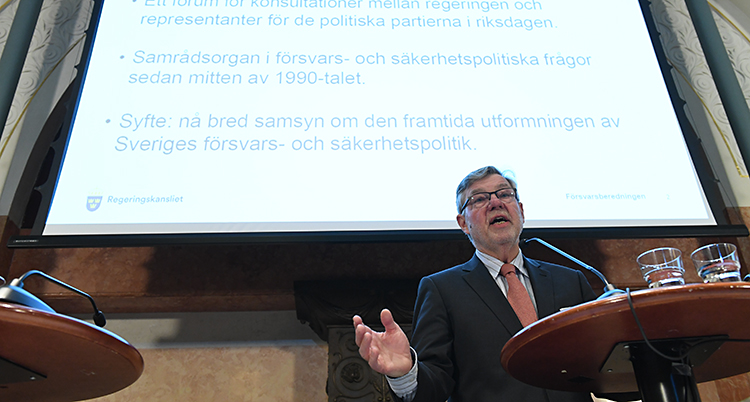 En man med slips framför en stor skärm med text