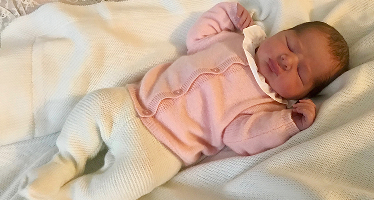 Den nyfödda prinsessan klädd i vita byxor och rosa kofta ligger på en bädd i vitt. Hon blundar.