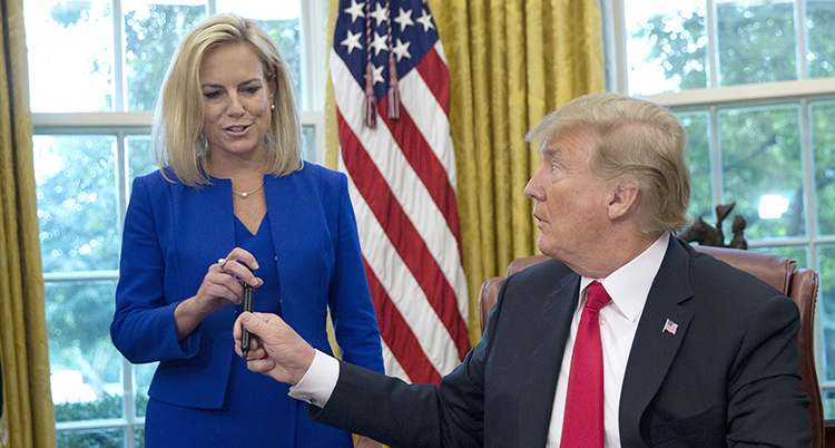 Trump vid sitt skrivbord i ovala rummet vänder sig mot Kirstjen NIelsen och ger henne en penna.