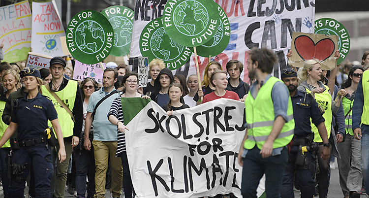 Ett demonstrationståg med Greta i första ledet. De längst fram bär en stor banderoll framför sig. Skolstrejk för klimatet står det.