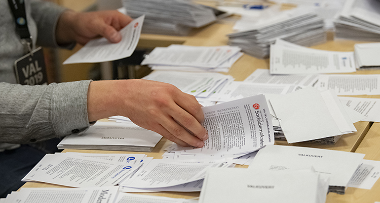 Man ser händerna på en person som bläddrar bland röstsedlar