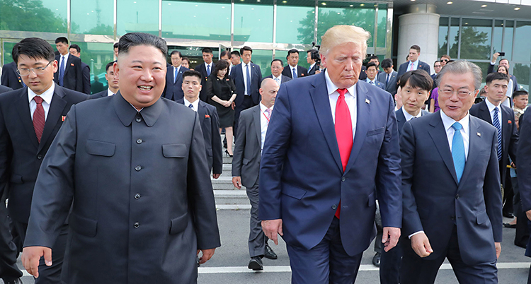 Kim och Trrump går bredvid varandra. Kim ler men Trump ser sur ut och tittar mot marken.