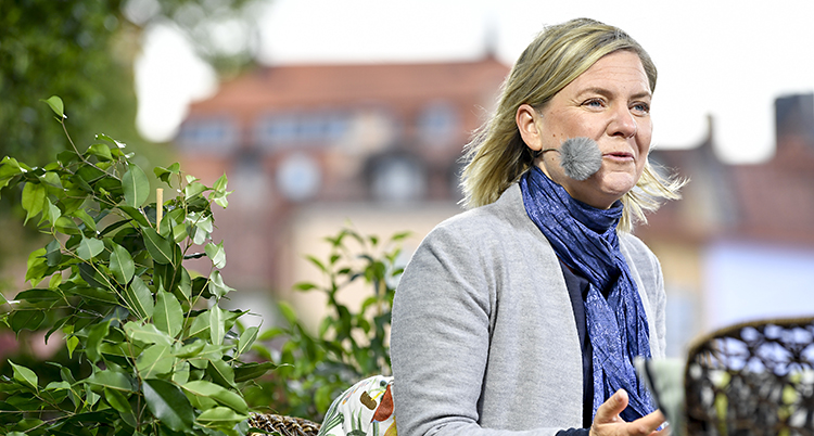 Magalena utomhus i blåst. Han står bland gröna växter och talar