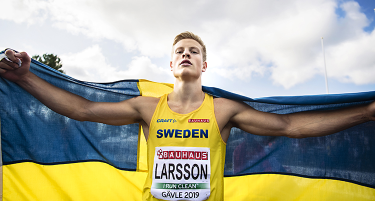 Friidrottaren Henrik Larsson håller en stor svensk flagga över ryggen.