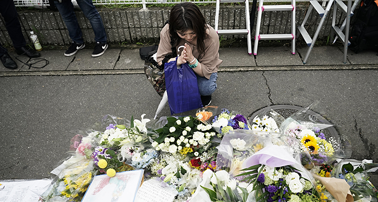 En kvinna knäböjer framför en hög med blombuketter på en trottoar.