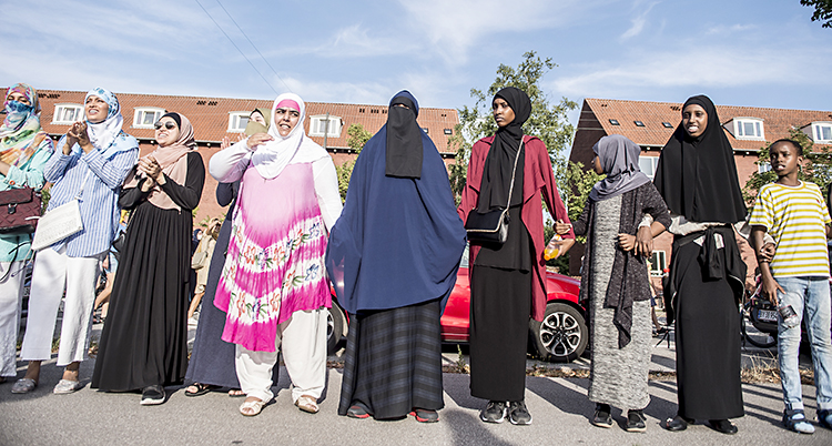 Människor på rad håller varandras händer. Flera har täckt håret eller hela kroppen med slöja