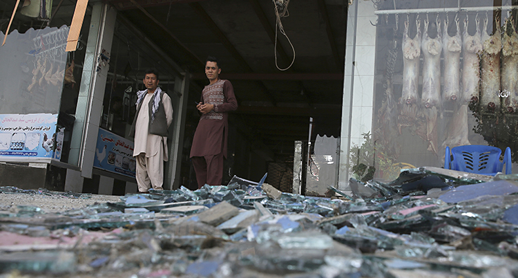 Två män står vid en affär i staden Kabul. På marken ligger en massa bråte efter en explosion.