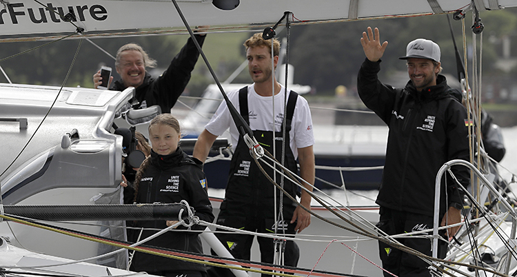 Greta och tre män på segelbåten. Greta ler, två av männen skrattar och vinkar.