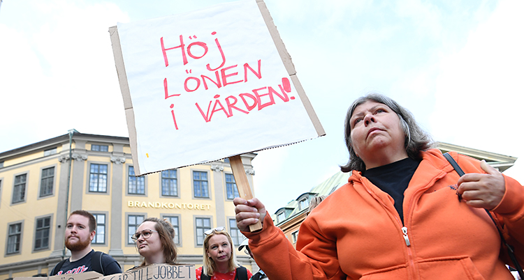 En sköterska med plaket där hon skrivit Höj lönen i vården.