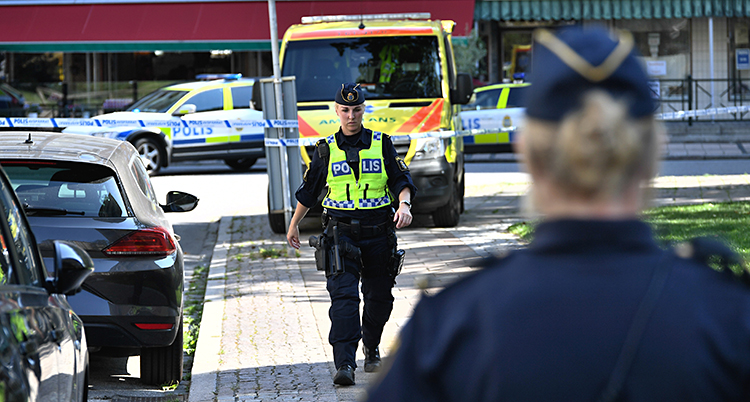 En polis nära fotografen, med ryggen mot kameran. Längre bort i bilden syns en annan polis med reflexväst som går mot fotografen. Längst bak i bilden syns en ambulans och flera polisbilar. Bilden är tagen i stadsmiljö i Malmö.