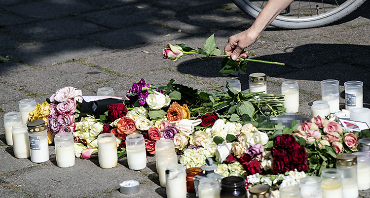 Blommor och ljus på marken. En hand ses lägga ner en ros.