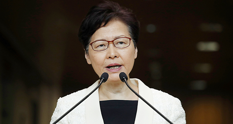Hongkongs ledare Carrie Lam pratar med journalister. Hon pratar in i två mikrofoner. Hon har glasögon på sig, en svart tröja och en vit kavaj.