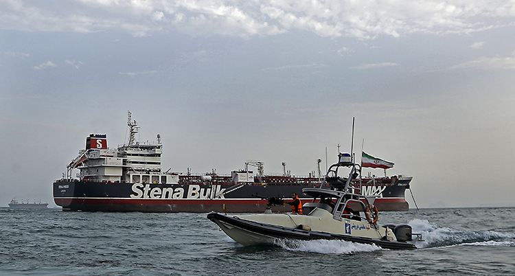 En mindre båt med militärer och iranska flaggor åker runt en stor båt som det står Stena Bulk på.