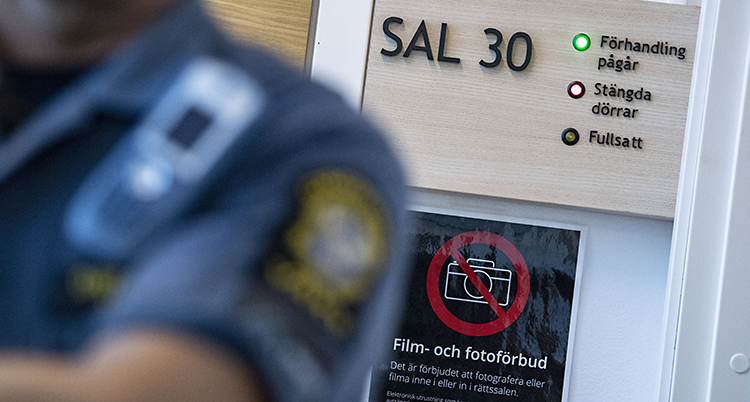 En ordningsvakt står närmast bilden. Det är bara axeln, bröstet och armen som syns. I bakgrund står det Sal 30. Bilden är tagen i en tingsrätt.