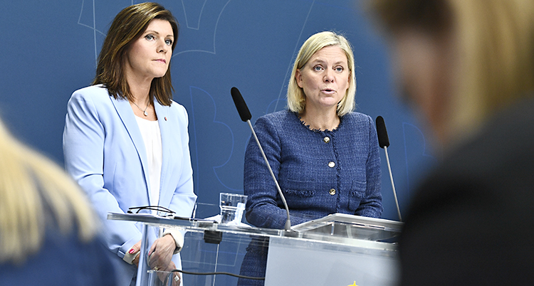 De har blåa kavajer och står bakom ett bord i riksdagen med mikrofoner framför sig