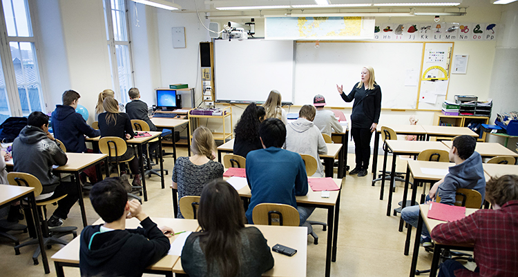 En lärare står längst fram i ett klassrum fyllt av elever