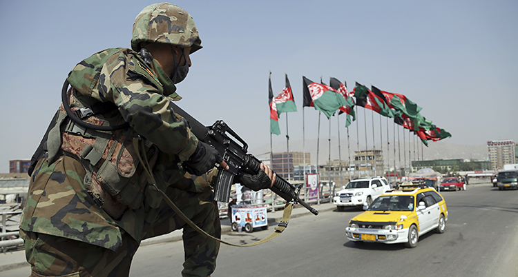 En soldat med vapen vaktar en gata med bilar och afghanska flaggor