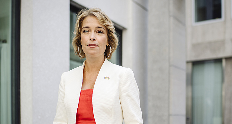 Politikern Annika Strandhäll står på en innergård. Hon tittar in i kameran. Hon har en röd tröja och en vit kavaj, och halvlångt hår.