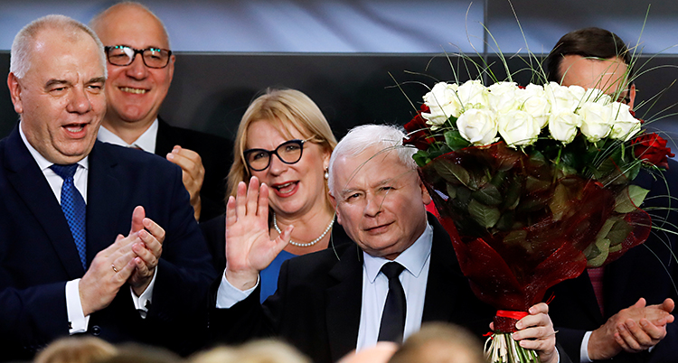 Partiet Lag och rättvisa vann stort i helgens val. Ledaren Jaroslaw Kaczynski vinkar med ena handen. I den andra har han en bukett vita rosor. Runt honom står flera andra glada politiker.