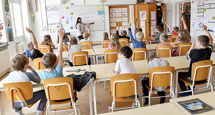 Elever sitter i ett klassrum och tittar mot läraren. Några räcker upp handen