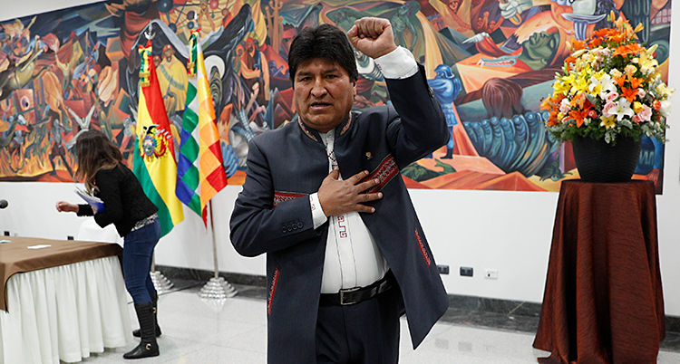 Evo Morales håller upp en arm. Han står framför en vägg målad i starka färger