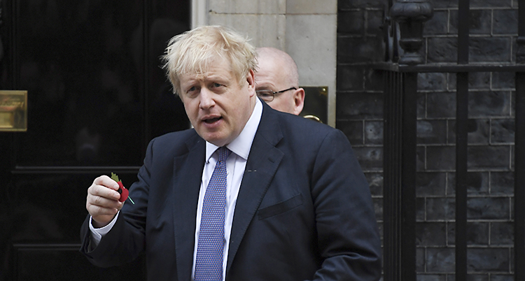 Boris Johnson har kostym och en blå slips. Han står framför en dörr.