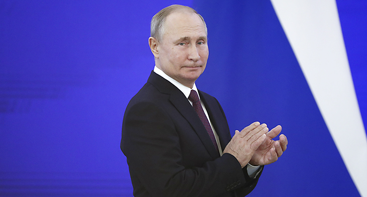 Vladimir Putin står framför en blå vägg och tittar åt sidan