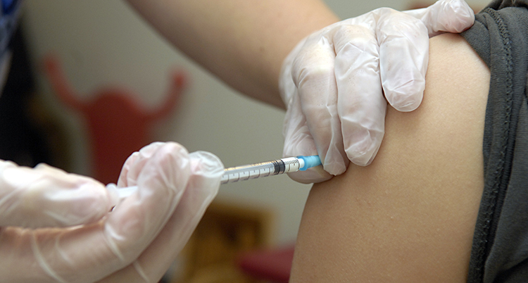 Händer med handskar sprutar in vaccin i en arm