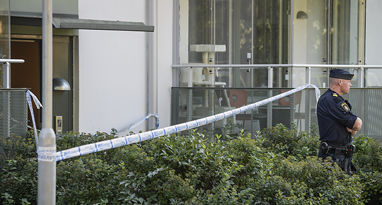 Poliser har spärrat av runt ett hus med lägenheter. Utanför huset står en polis och vaktar.