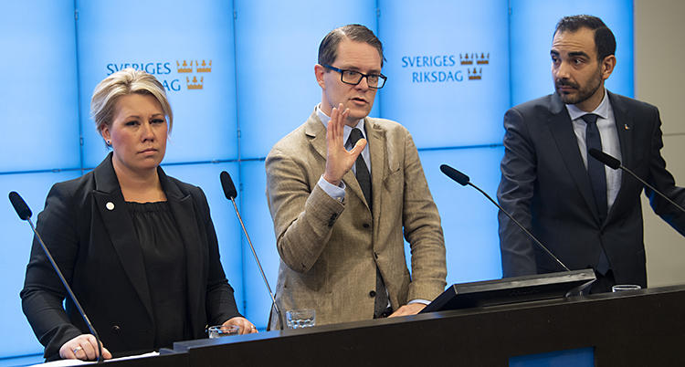 Tre politiker står bredvid varandra. De är i ett rum i riksdagen. De pratar för journalister.