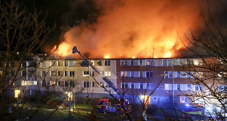 Det är mörkt och stora lågor slår upp från taket på ett stort hus.