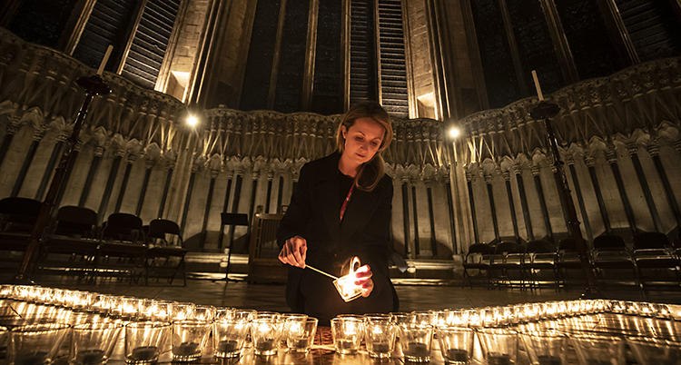 Bilden är från en kyrka i York i Storbritannien. En kvinna tänder ett ljus. Det finns en massa tända ljus runt henne.