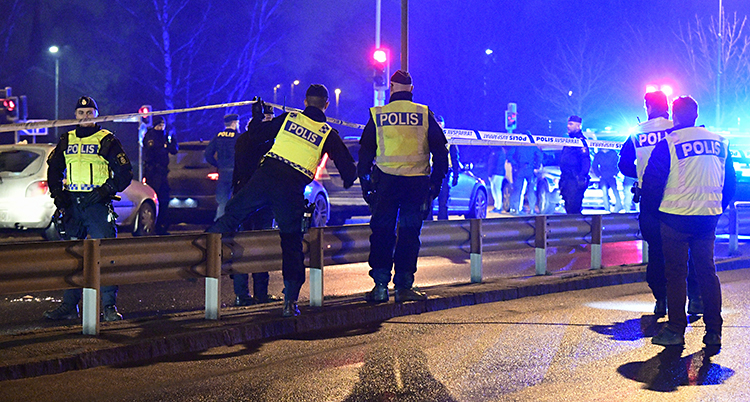 Poliser stoppar bilar vid en vägkant. Det är kväll på bilden.