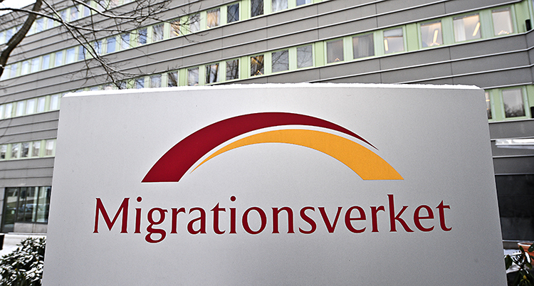 En stor skylt där det står Migrationsverket. I bakgrunden syns ett stort grått hus.