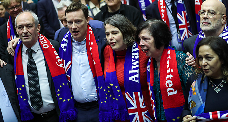 Politiker står i EUs riksdag i Bryssel. De har halsdukar på sig med Storbritanniens flagga och EUs flagga.