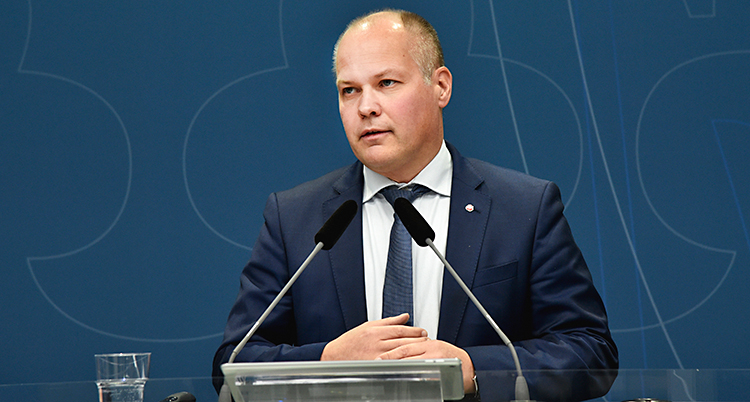 Morgan Johansson i blå kavaj och blå slips mot vit skjorta talar i två mikrofoner vid ett pressmöte.